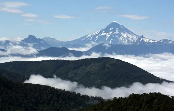 Cordillera nevada sobre un mar de nubes y bosque
