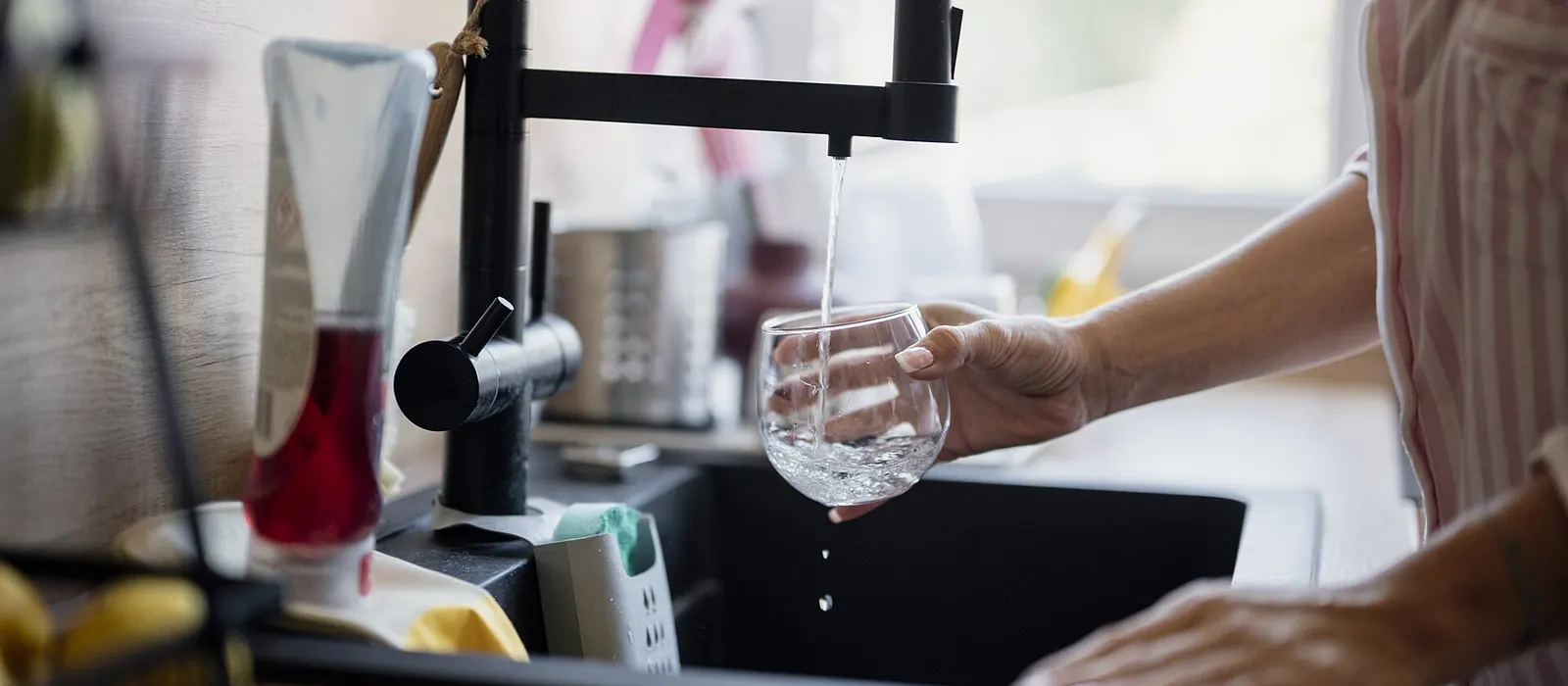 Persona llenando un vaso con agua de la llave en la cocina de su casa